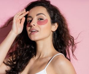 Pretty woman with hydrogel eye patches touching forehead on pink background / envato